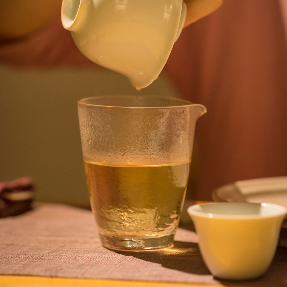 pouring infused tea into glass with white tea pot